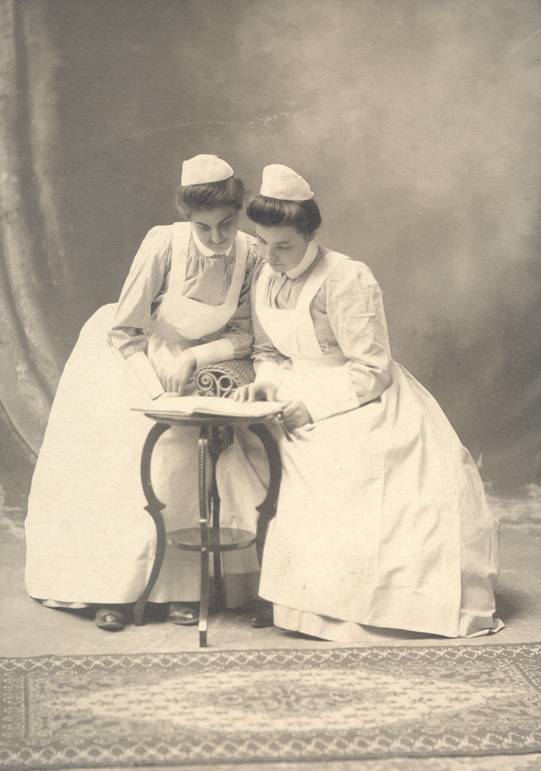 two nurses look at a book on a table