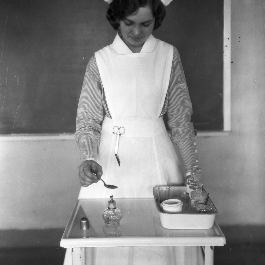 nurse in white cap and apron spooning medicine