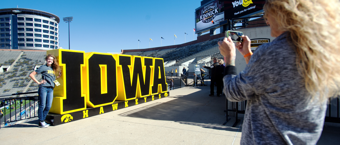 A student standing next to the Iowa Hawkeyes sign